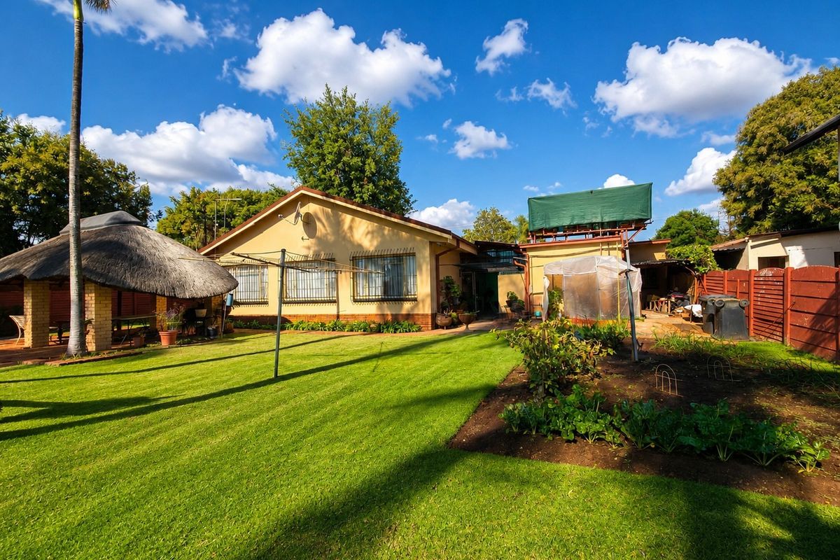 Rear view of the property featuring a spacious lawn, a traditional thatched lapa, and a vegetable garden area.