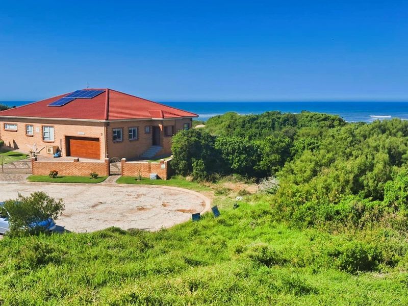 Aerial view of a residential property featuring a brick home with solar panels, a tiled roof, and a garage, situated near the coastline.
