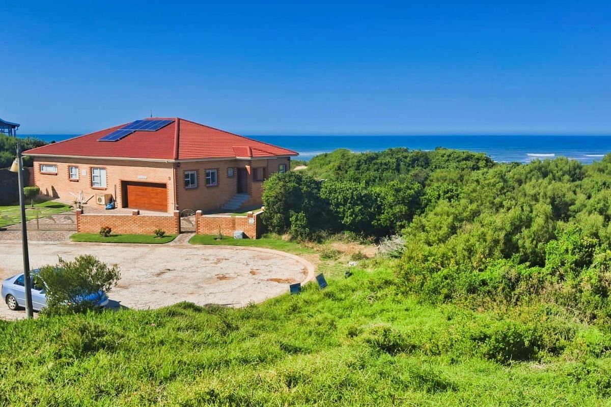 Aerial view of a residential property featuring a brick home with solar panels, a tiled roof, and a garage, situated near the coastline.