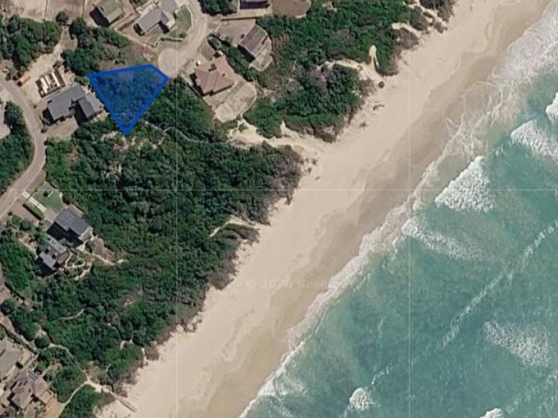 Aerial view of a vacant residential plot situated in a coastal neighborhood with direct proximity to the beach and natural vegetation.