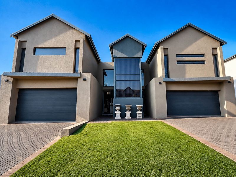Modern double-story residential property featuring a symmetrical facade, dual garages, paved driveway, and a central glass-paneled entrance.