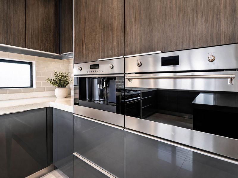 Modern kitchen featuring high-gloss and wood veneer cabinetry, stone countertops, subway tile backsplash, and integrated stainless steel appliances including an oven and coffee machine.