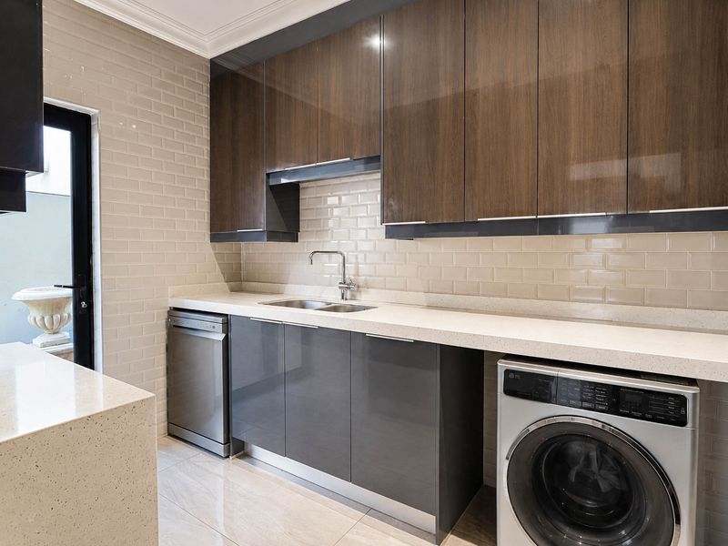 Modern laundry room featuring sleek dark cabinetry, stone countertops, subway tile backsplash, and integrated appliances including a dishwasher and washing machine.