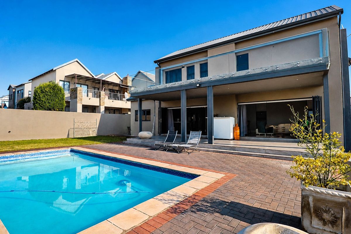 Rear exterior view featuring a swimming pool, paved patio area, and a covered terrace with glass balustrades and large bi-fold doors.