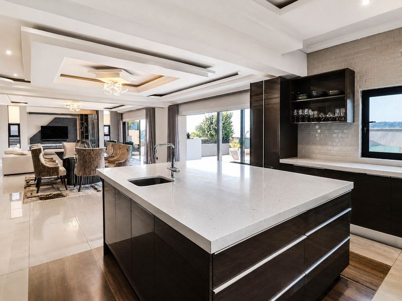 Modern open-plan kitchen and living area featuring a large stone-topped island, sleek dark cabinetry, recessed ceiling details, and seamless flow to an outdoor patio.