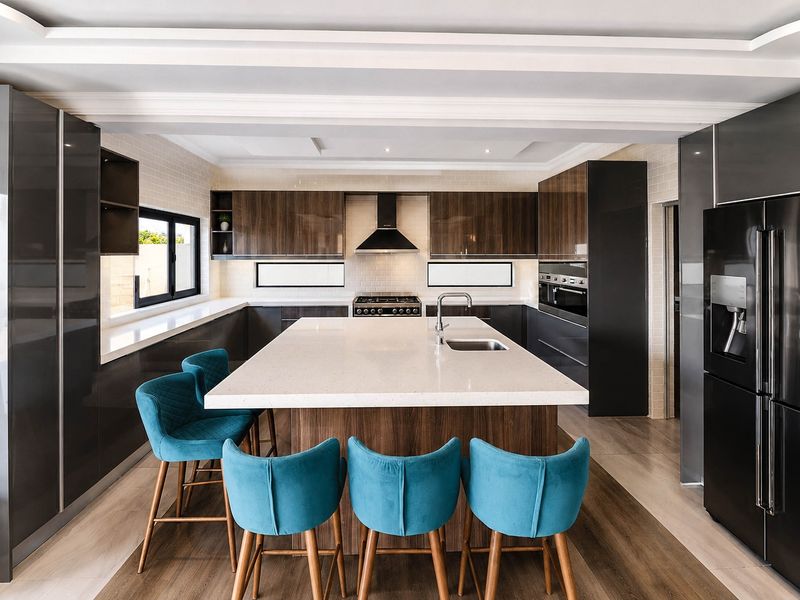 Modern kitchen featuring a large central island with quartz countertops, high-gloss cabinetry, built-in appliances, and sleek contemporary finishes.