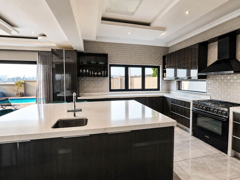 Modern kitchen featuring a large island with stone countertops, dark cabinetry, high-end gas range, and subway tile backsplash, opening to an outdoor pool area.