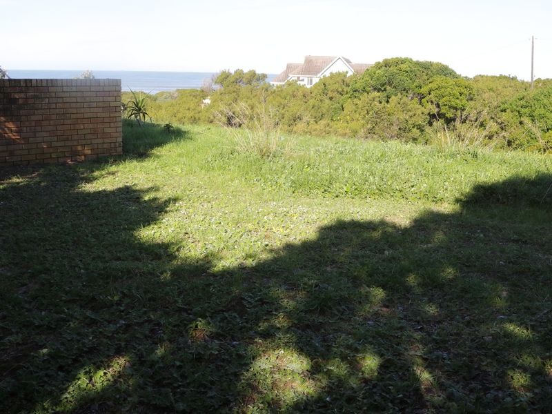 A view of the vacant residential land featuring a brick boundary wall and natural vegetation with a distant ocean view.