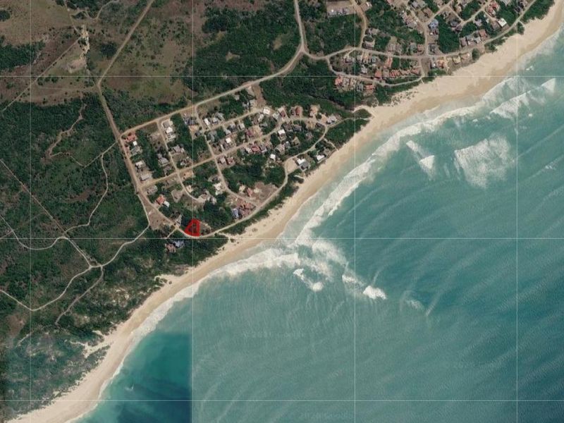 Aerial view of a coastal residential plot highlighted in red, situated near the beach in a scenic seaside neighborhood.