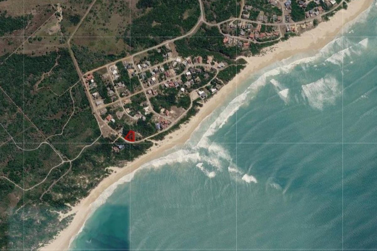 Aerial view of a coastal residential plot highlighted in red, situated near the beach in a scenic seaside neighborhood.