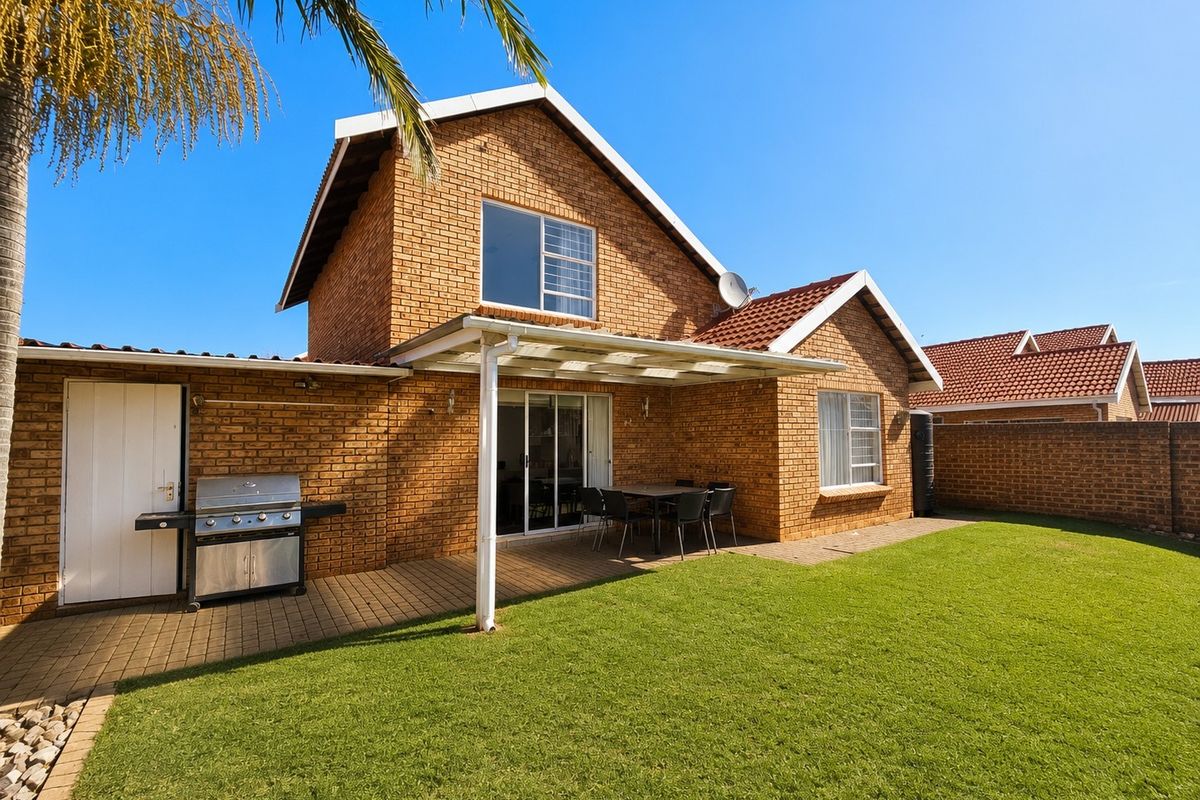 Rear view of a brick house featuring a covered patio, paved outdoor area, and a well-maintained lawn.