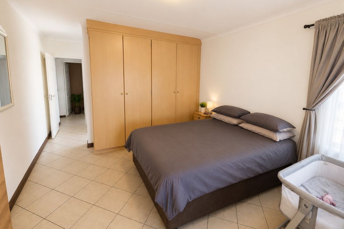 A well-maintained bedroom featuring neutral tiled flooring, a large built-in wooden wardrobe, and natural light through the window.