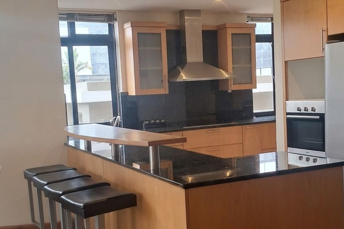 Modern kitchen featuring wooden cabinetry, granite countertops, a breakfast bar, and integrated stainless steel appliances, illuminated by recessed downlights.