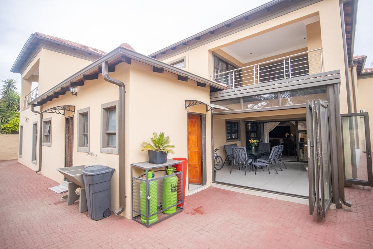 Rear view of the property featuring a paved patio, folding glass doors leading to the interior, and an upper-level balcony with stainless steel railings.