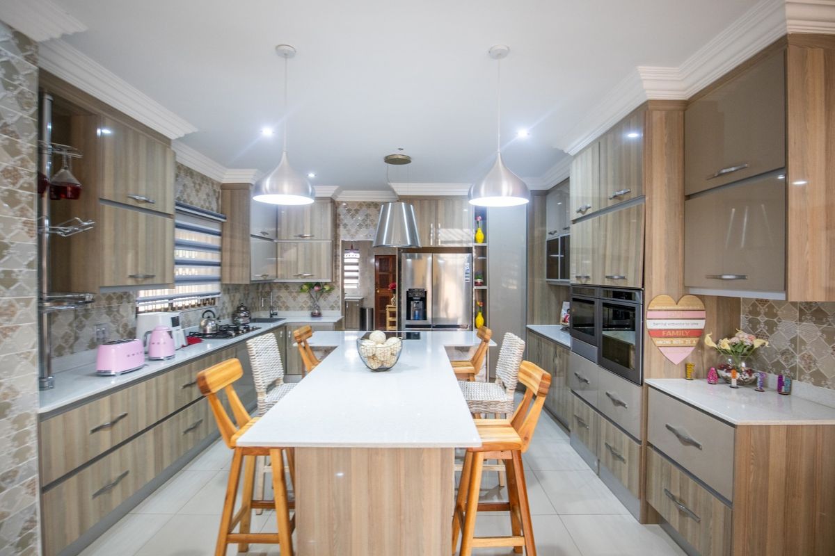 Modern kitchen featuring extensive wood-finish cabinetry, a central island with stone countertops, integrated double ovens, and stylish pendant lighting.