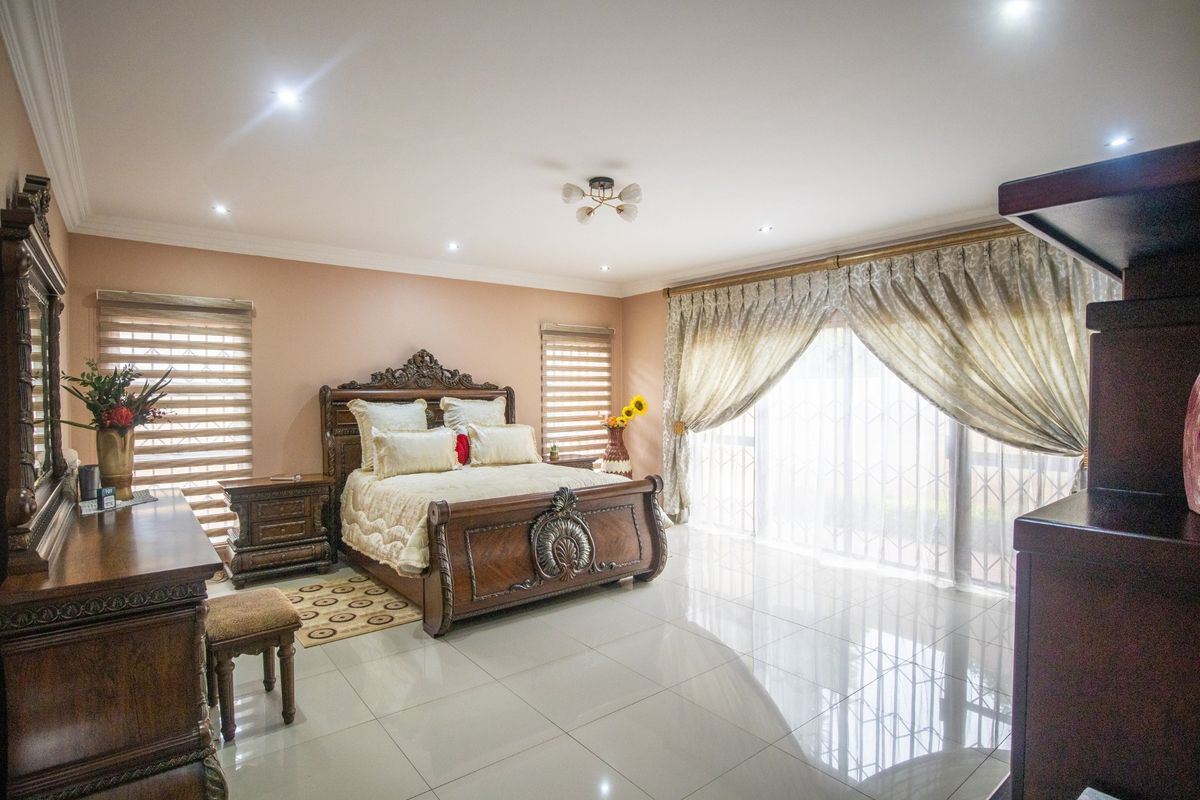 Spacious bedroom featuring polished porcelain floor tiles, recessed downlighting, and large sliding glass doors with integrated security gates leading to the exterior.