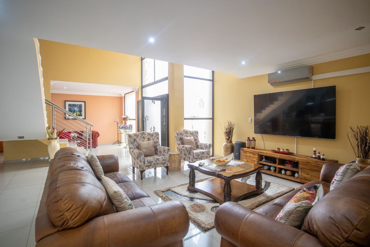 Spacious living room featuring high ceilings, large windows for natural light, tiled flooring, and a split-system air conditioner.