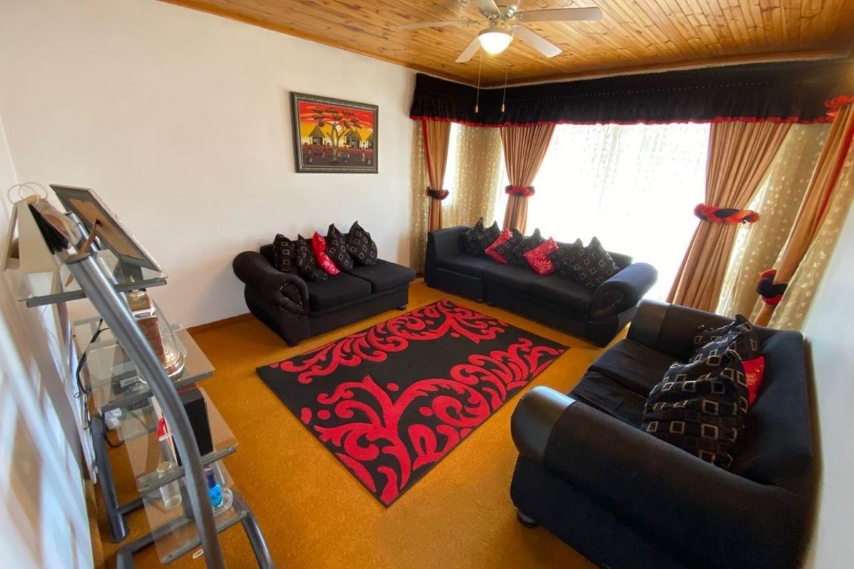 A living room featuring a timber tongue and groove ceiling, ceiling fan, and carpeted flooring, offering a traditional aesthetic.