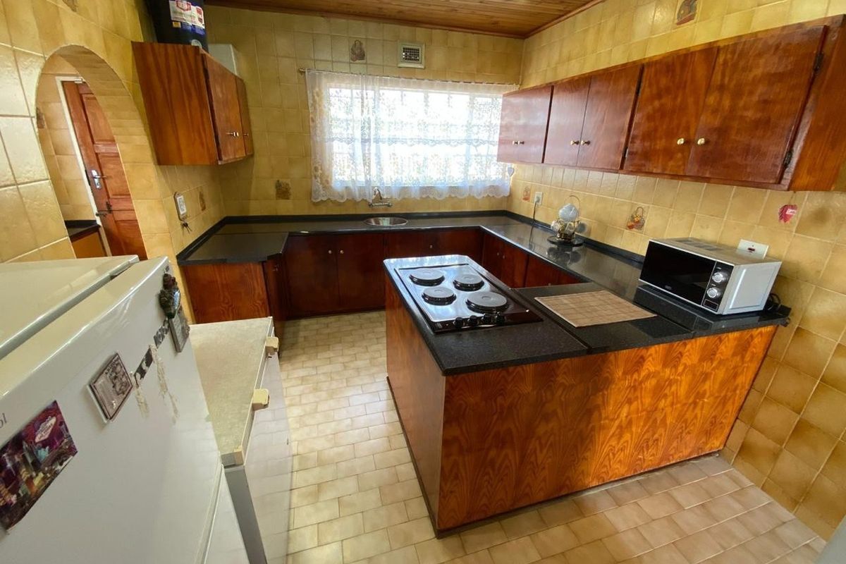 A functional kitchen featuring wooden cabinetry, stone countertops, a built-in hob, and tiled splashbacks with a timber ceiling finish.