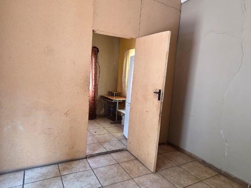 An empty bedroom featuring tiled flooring and visible wall damage, requiring cosmetic repairs and refurbishment to restore the space.