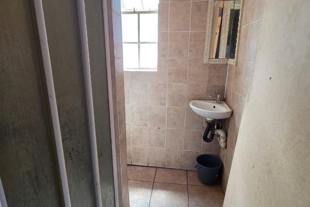 A small, dated bathroom featuring a wall-mounted basin, tiled surfaces, and a shower enclosure, currently in need of renovation and cosmetic updates.