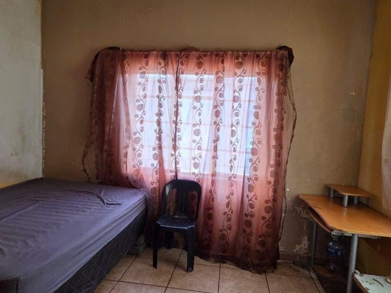 A bedroom featuring tiled flooring and a window, currently requiring cosmetic updates to the wall finishes and general maintenance.