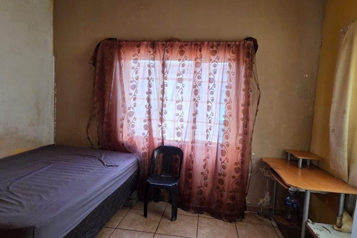 A bedroom featuring tiled flooring and a window, currently requiring cosmetic updates to the wall finishes and general maintenance.