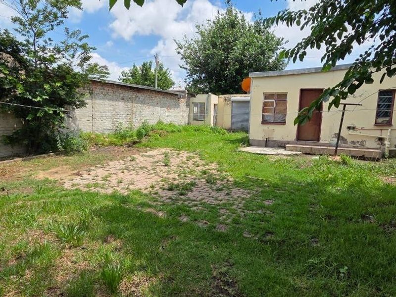 Rear exterior view of the property featuring a large garden area, brick boundary walls, and a small outbuilding structure requiring maintenance.