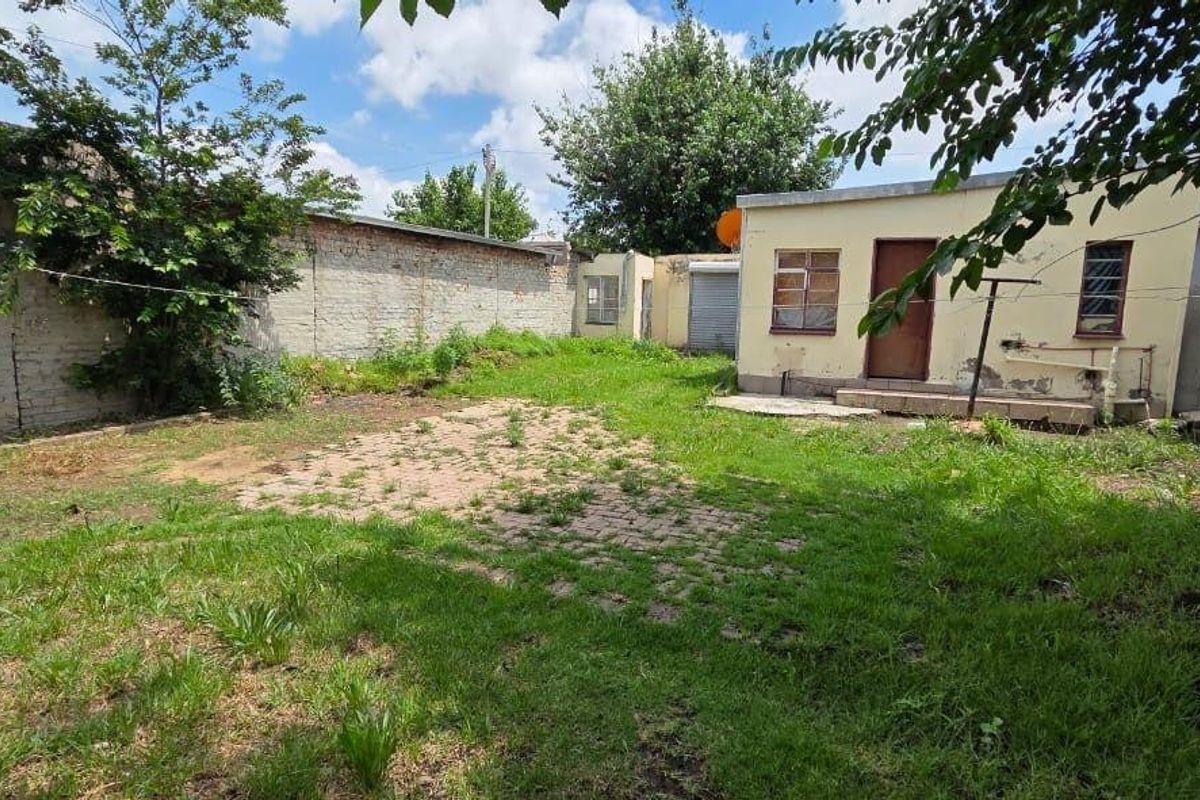 Rear exterior view of the property featuring a large garden area, brick boundary walls, and a small outbuilding structure requiring maintenance.