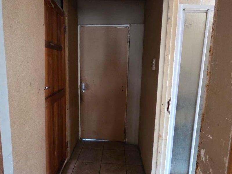 A narrow interior hallway featuring tiled flooring and multiple wooden door frames, currently requiring cosmetic repairs and finishing to the wall surfaces.