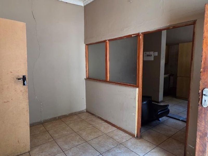 An empty hallway featuring tiled flooring, a timber door, and an internal glass partition, showing visible wall cracking and signs of wear.