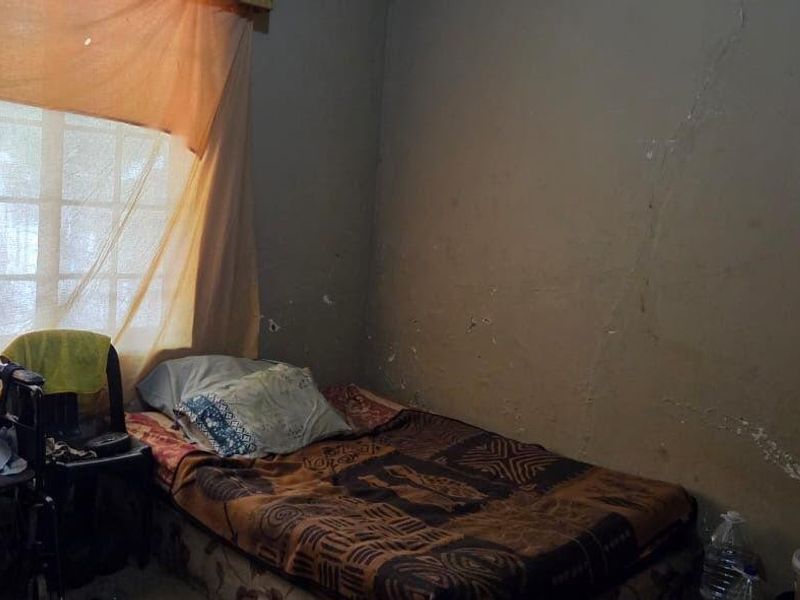 A bedroom featuring a grid-pane window, currently showing significant wear to the wall finishes including cracking and peeling paint.