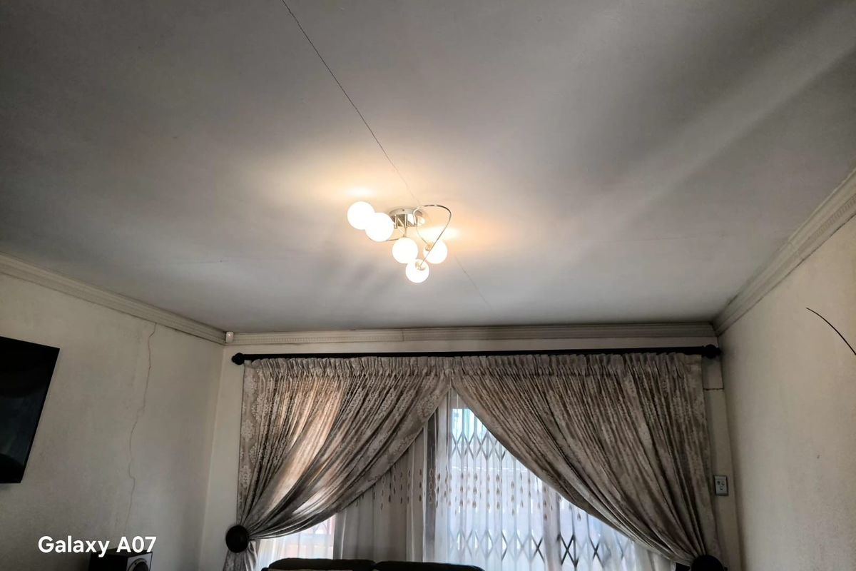 A living room area featuring a ceiling light fixture, decorative cornice, and a security gate over the window.