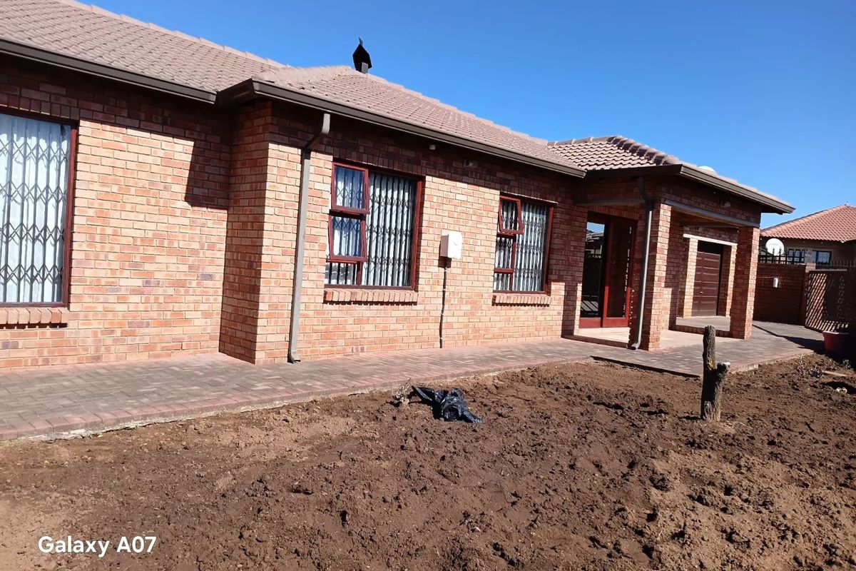 Rear view of a face brick house featuring a tiled roof, security gates, and a paved walkway leading to an unlandscaped garden area.