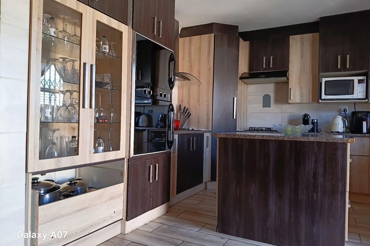 Modern kitchen featuring two-tone cabinetry, granite countertops, built-in oven, extractor fan, and glass-front display units with tiled flooring.