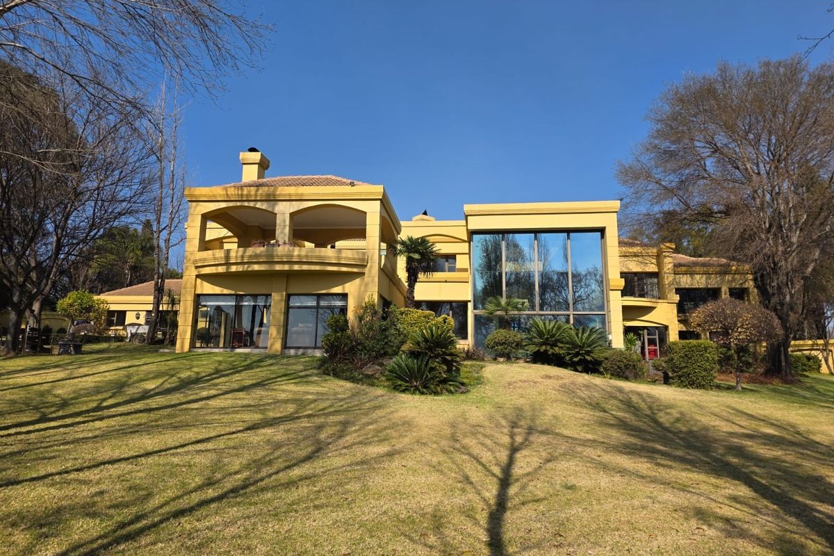 Rear view of a large multi-story residence featuring a spacious lawn, expansive glass windows, and a covered balcony area.
