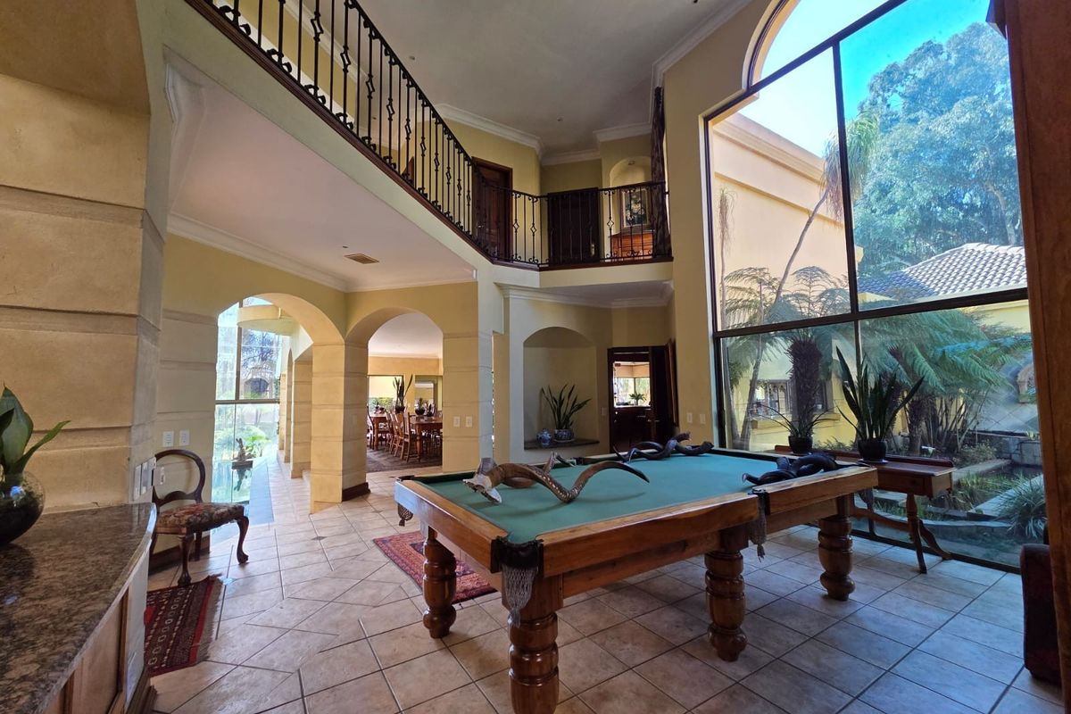 Spacious double-volume living area featuring a mezzanine level, wrought iron balustrades, and expansive floor-to-ceiling windows overlooking the garden.