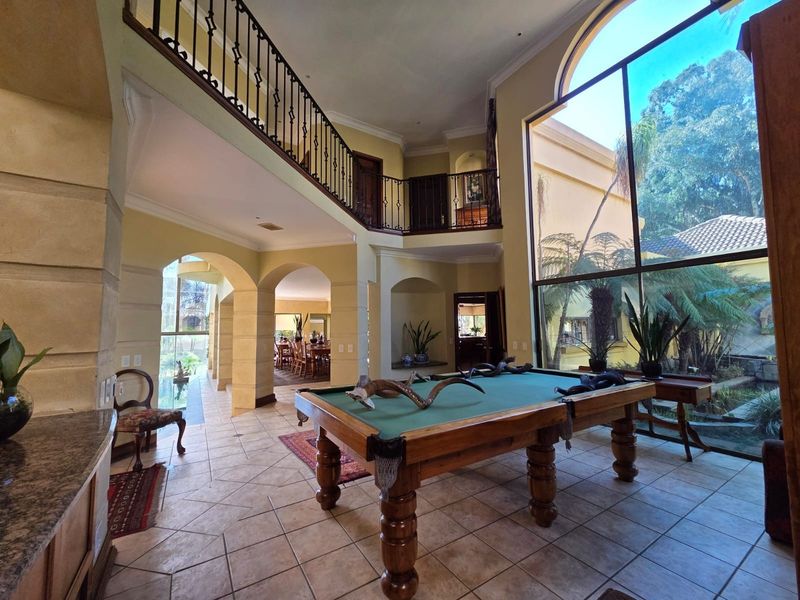 Spacious double-volume living area featuring a mezzanine level, wrought iron balustrades, and expansive floor-to-ceiling windows overlooking the garden.