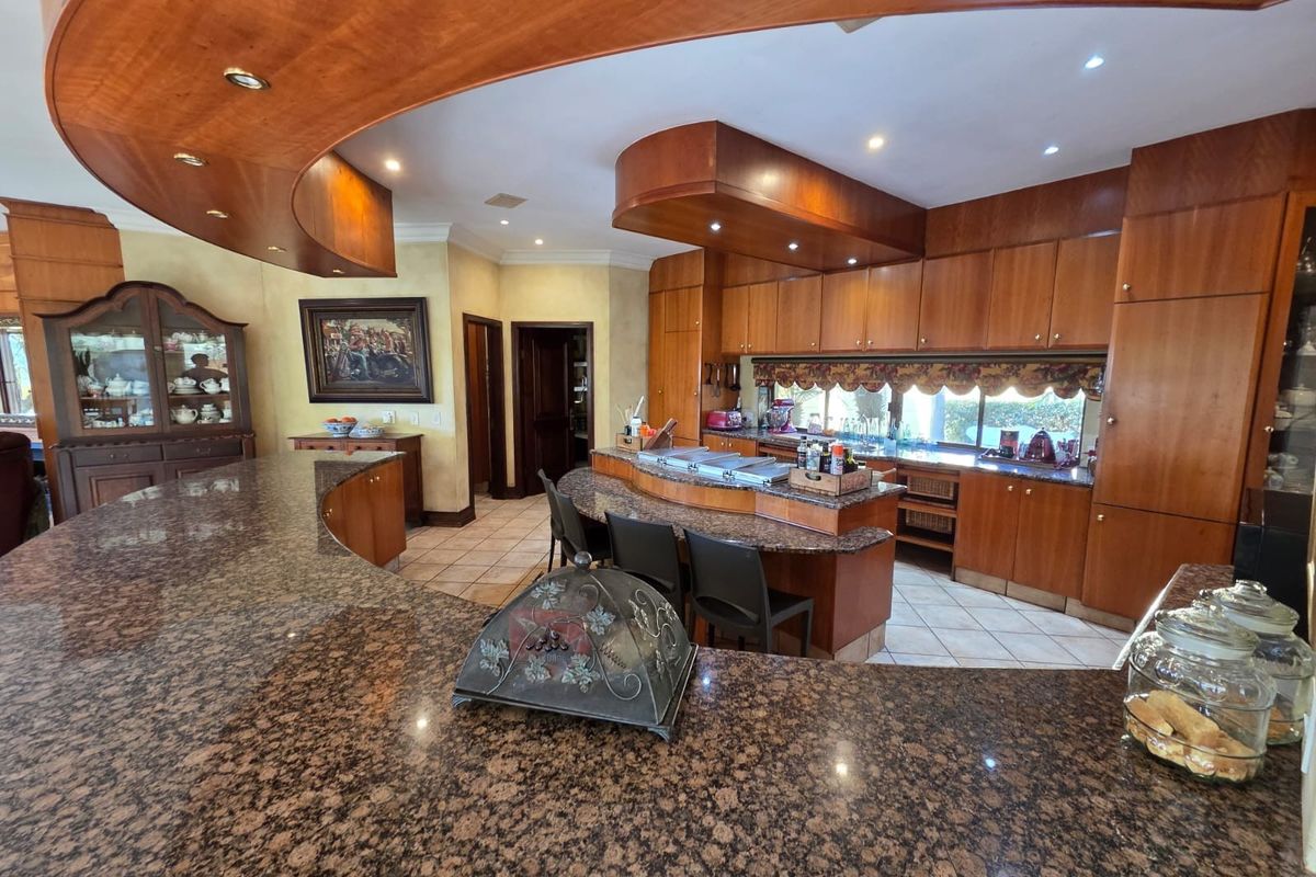 Spacious kitchen featuring extensive granite countertops, custom wooden cabinetry, and a unique curved bulkhead with integrated lighting, offering a functional and traditional layout.