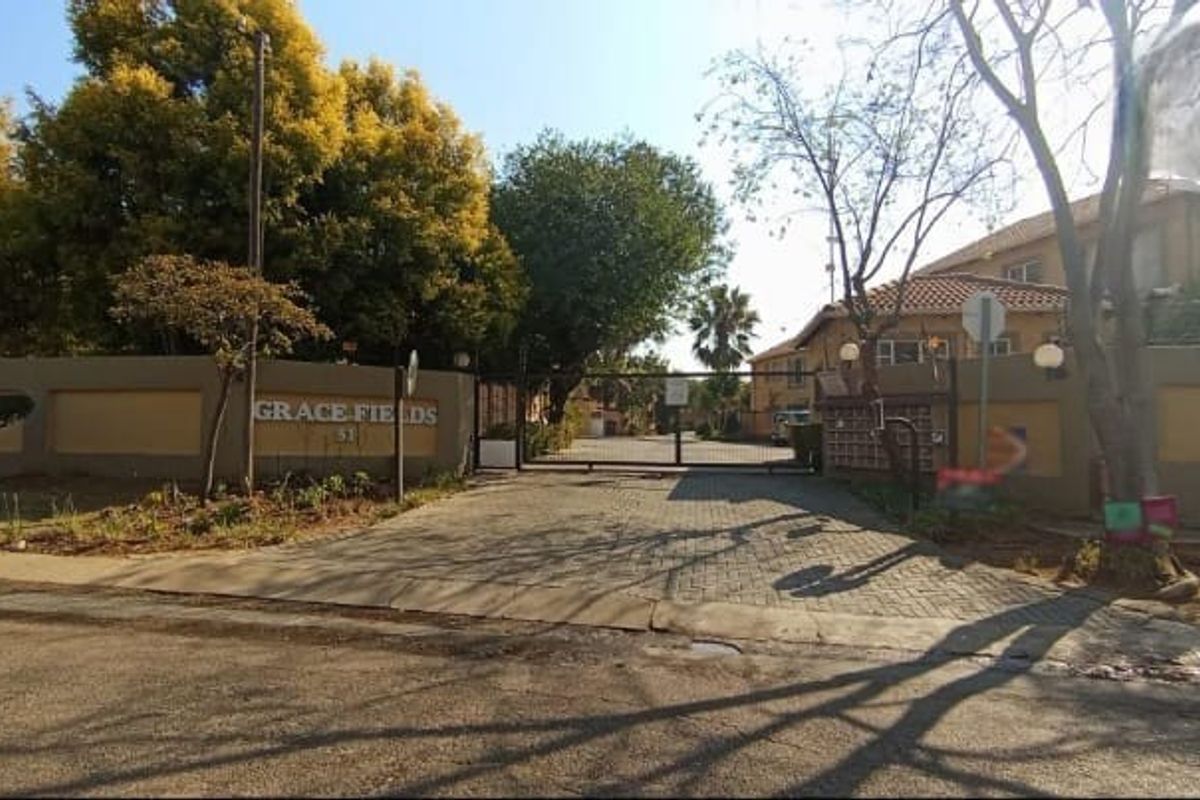 Street view of the Grace Fields townhouse complex entrance, featuring a secure gated access point, perimeter walling, and paved driveway.
