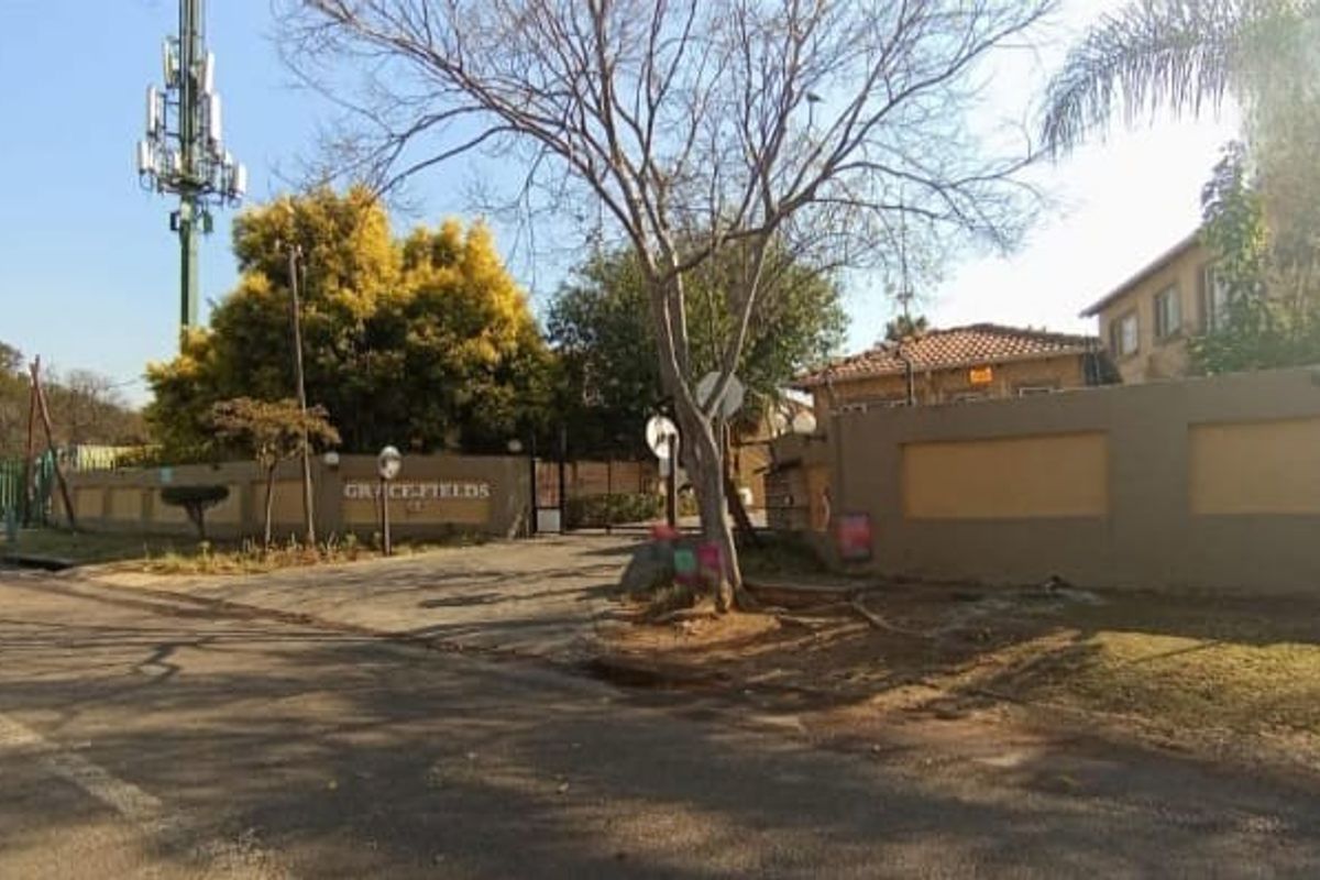 Street view of the Grace Fields townhouse complex entrance, featuring a perimeter wall and a prominent telecommunications mast.