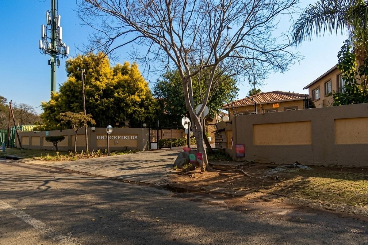 Street view of the Gracefields townhouse complex entrance, featuring a perimeter wall, security gate, and paved driveway access.