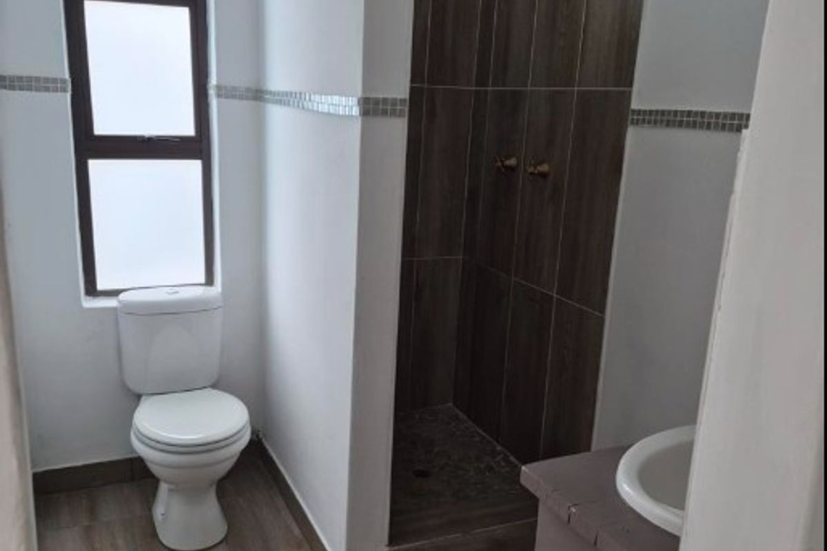 A clean, modern bathroom featuring a walk-in shower with wood-look tiling, a pedestal vanity, and a toilet, finished with neutral wall tones.