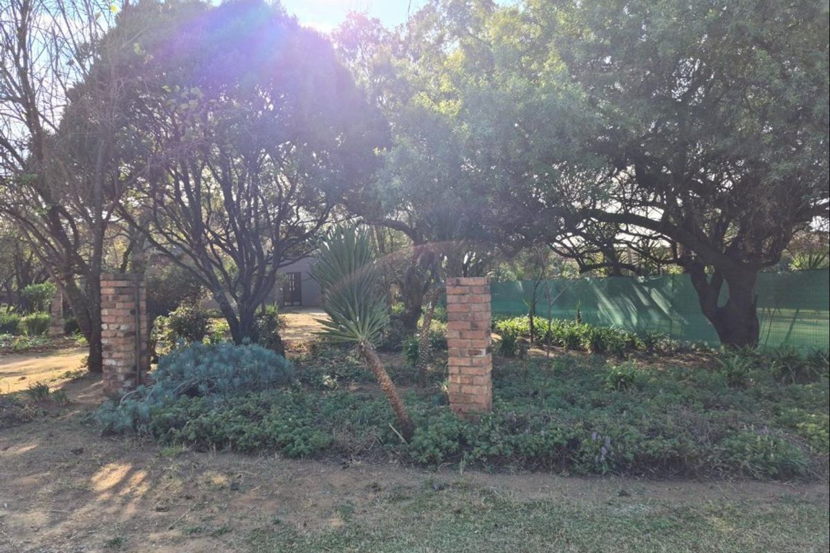 A mature garden area featuring established trees, landscaped ground cover, and decorative brick pillars, providing a natural and private outdoor setting.