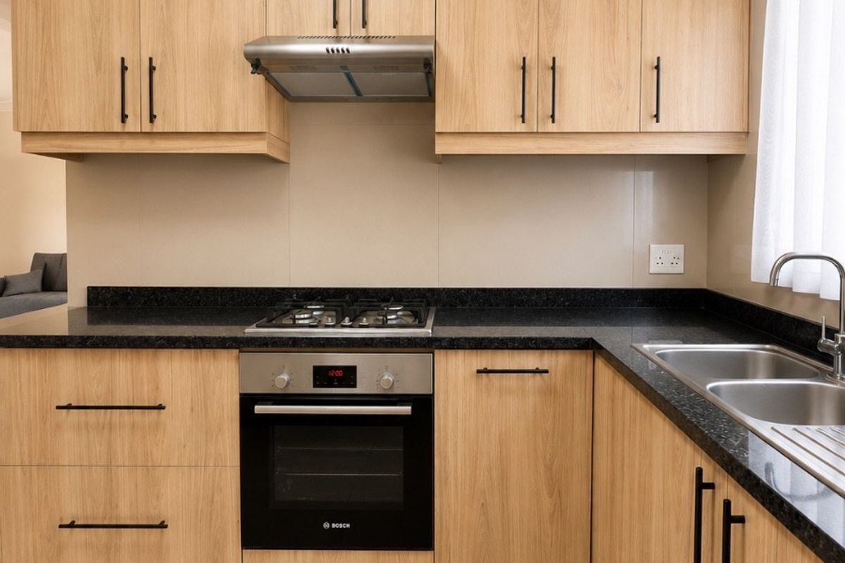 Modern kitchen featuring light wood-grain cabinetry, dark granite countertops, stainless steel appliances, and tiled flooring.