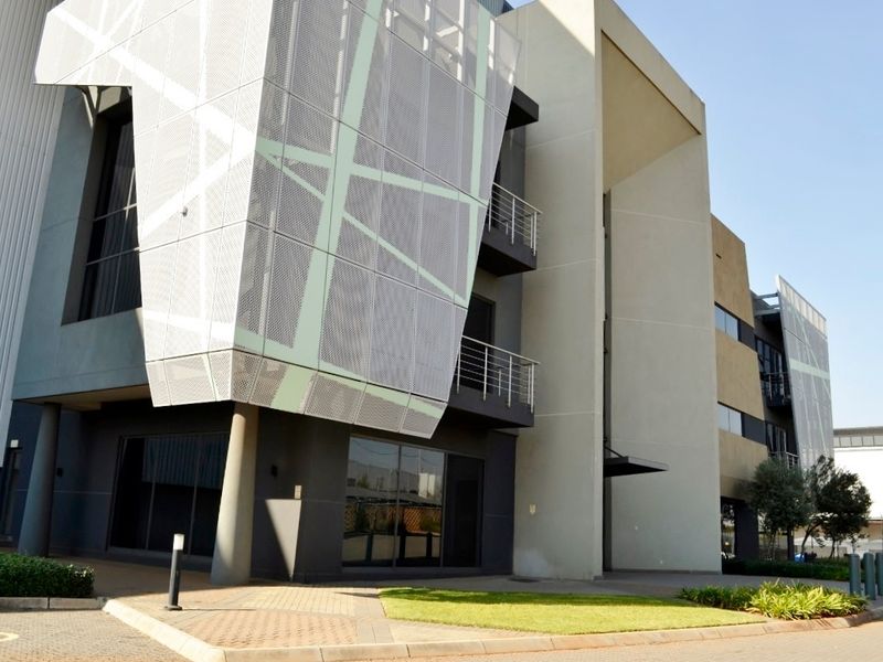 Modern industrial office building featuring a striking perforated metal facade, concrete structural elements, and integrated balconies with clean architectural lines.