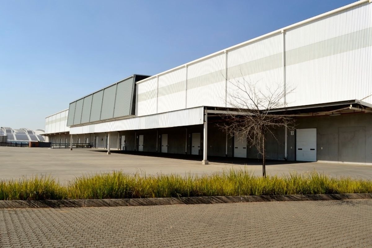 A large industrial warehouse facility featuring extensive corrugated metal cladding, multiple roller shutter loading doors, and a spacious concrete loading apron.