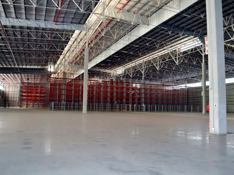 Spacious industrial warehouse featuring high ceilings with exposed steel trusses, polished concrete flooring, and an extensive built-in racking system for storage.