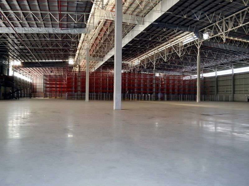 Expansive industrial warehouse space featuring high ceilings, polished concrete flooring, steel truss roofing, and integrated industrial racking systems.