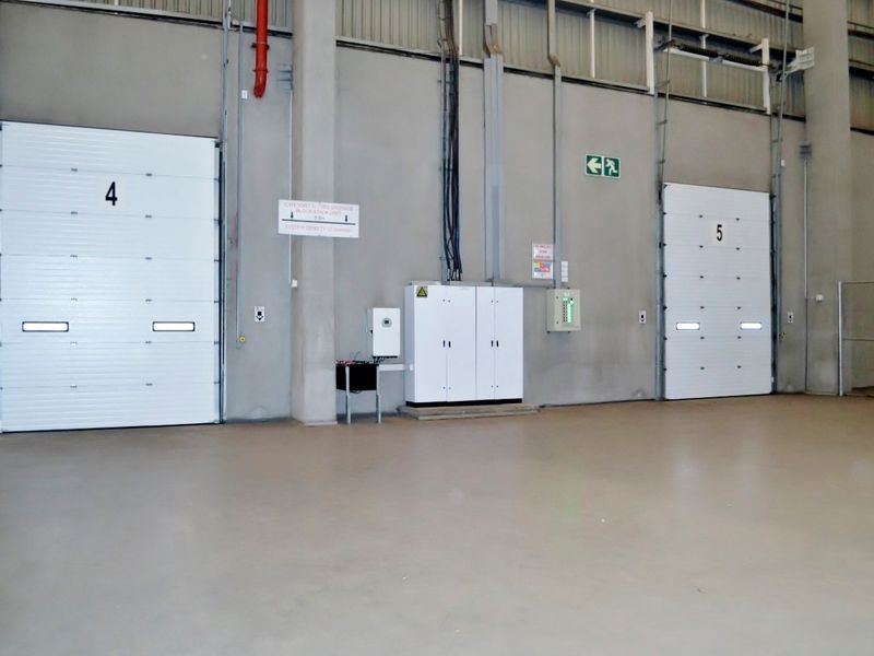 Spacious industrial warehouse interior featuring high ceilings, concrete flooring, and two numbered roller shutter loading doors with integrated electrical and fire safety infrastructure.